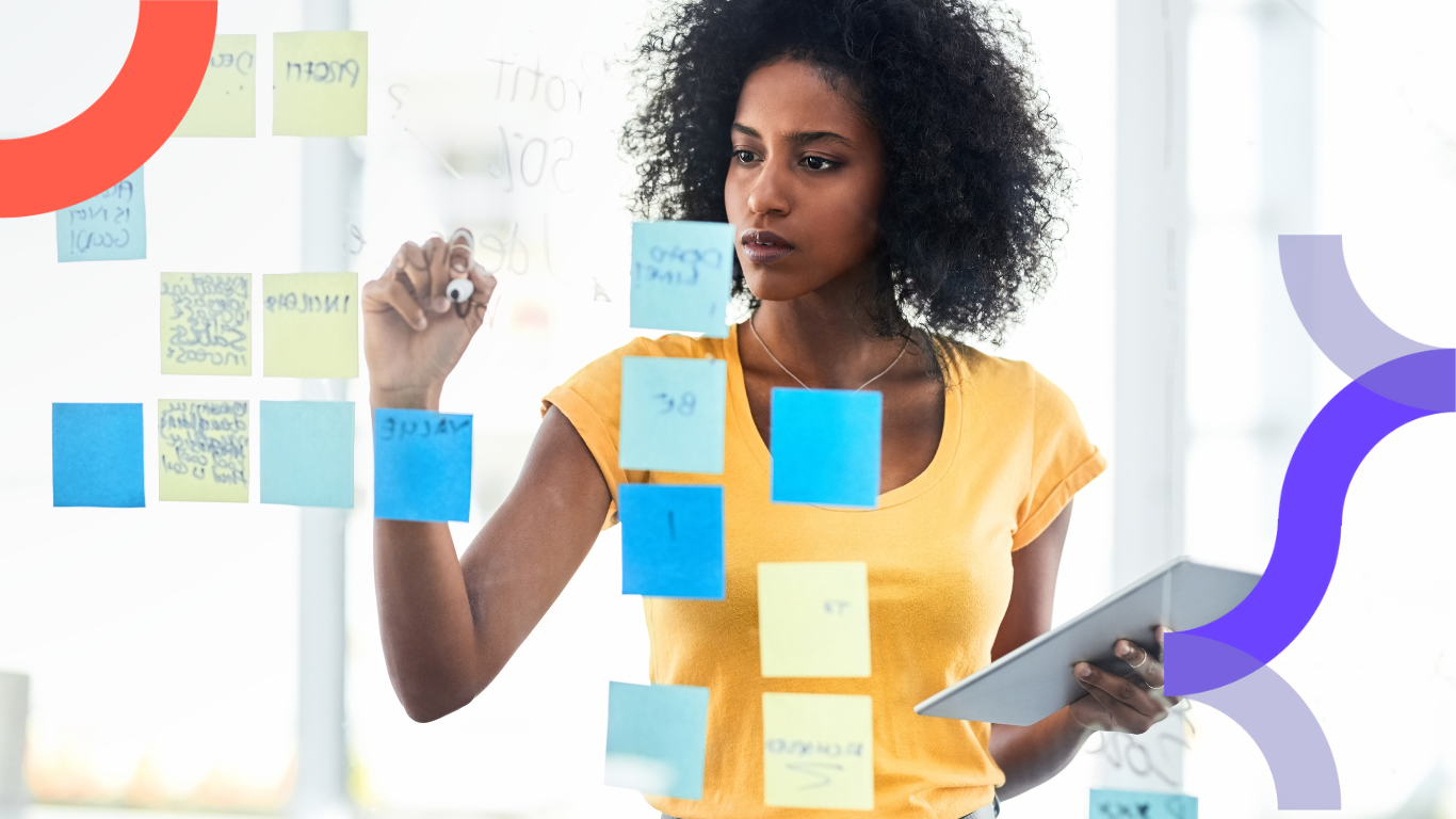 A woman stands behind a glass board with post it notes on it and writes content marketing tips on them